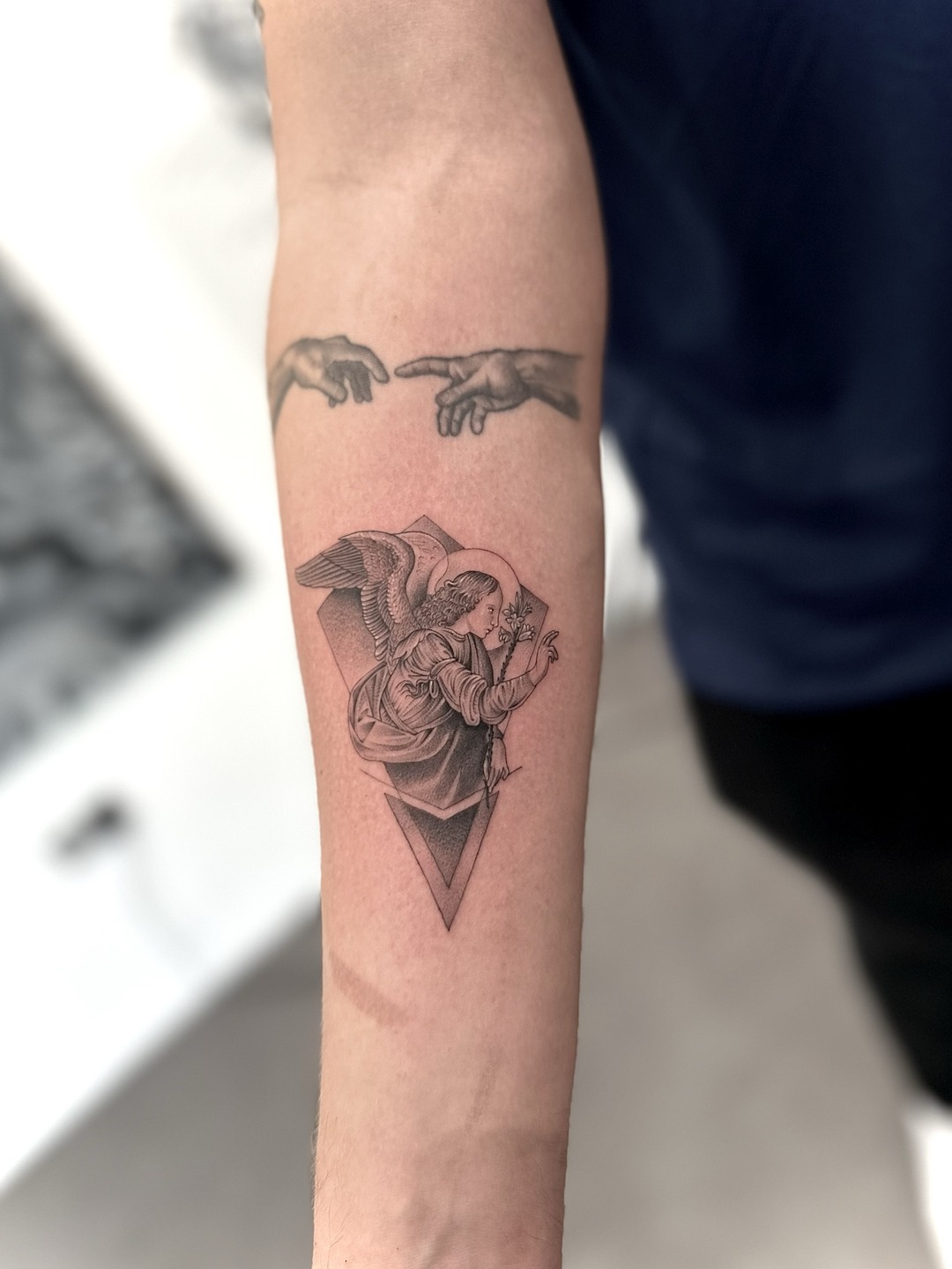 Annunciation angel with lily, fine line and geometric, forearm tattoo, black and grey by Matt Roe, Kensington London