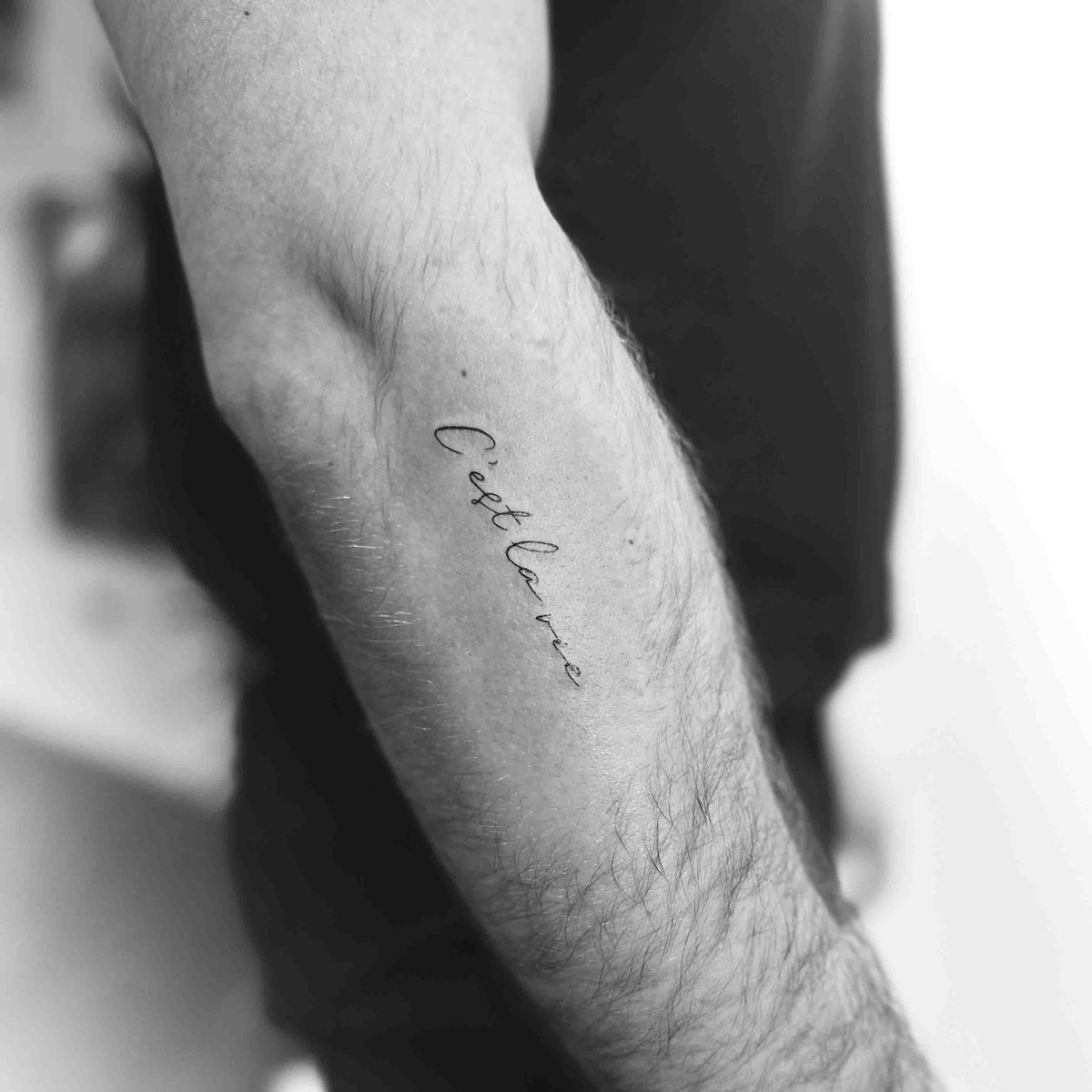 Delicate cursive French phrase tattoo on forearm by Matt Roe, Kensington London