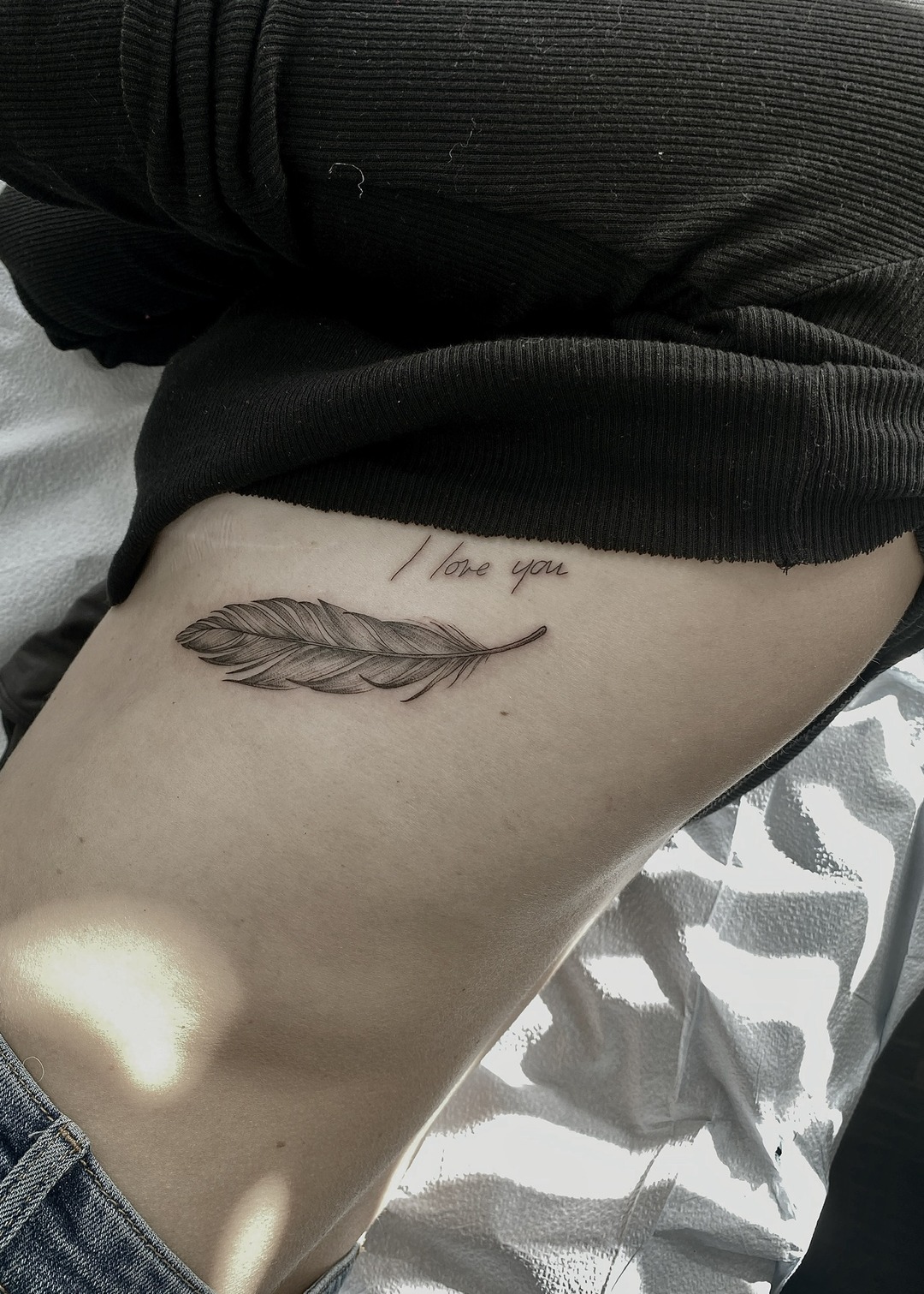 Feather with I love you script, ribs tattoo, black and grey by Matt Roe, Kensington London