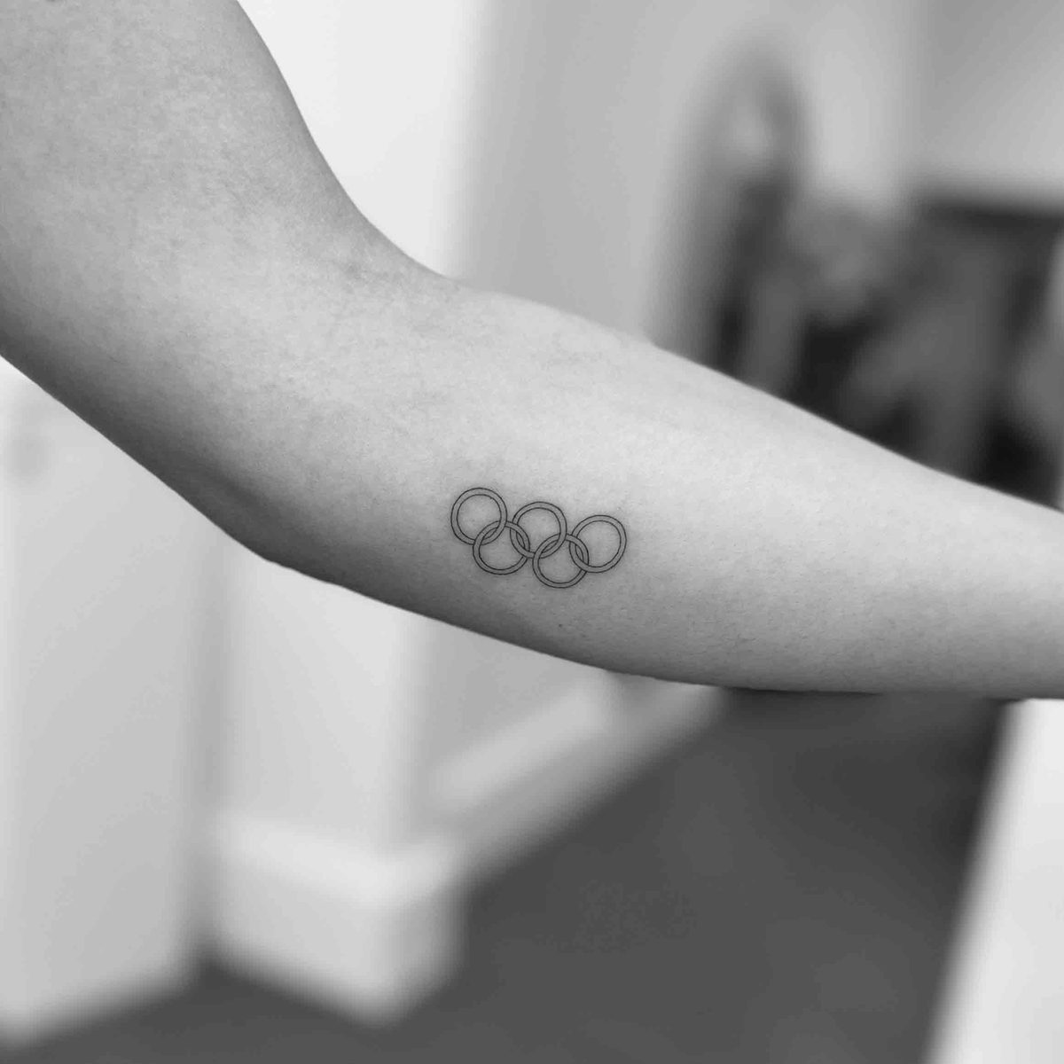 Fine line Olympic rings tattoo on forearm by Matt Roe, London