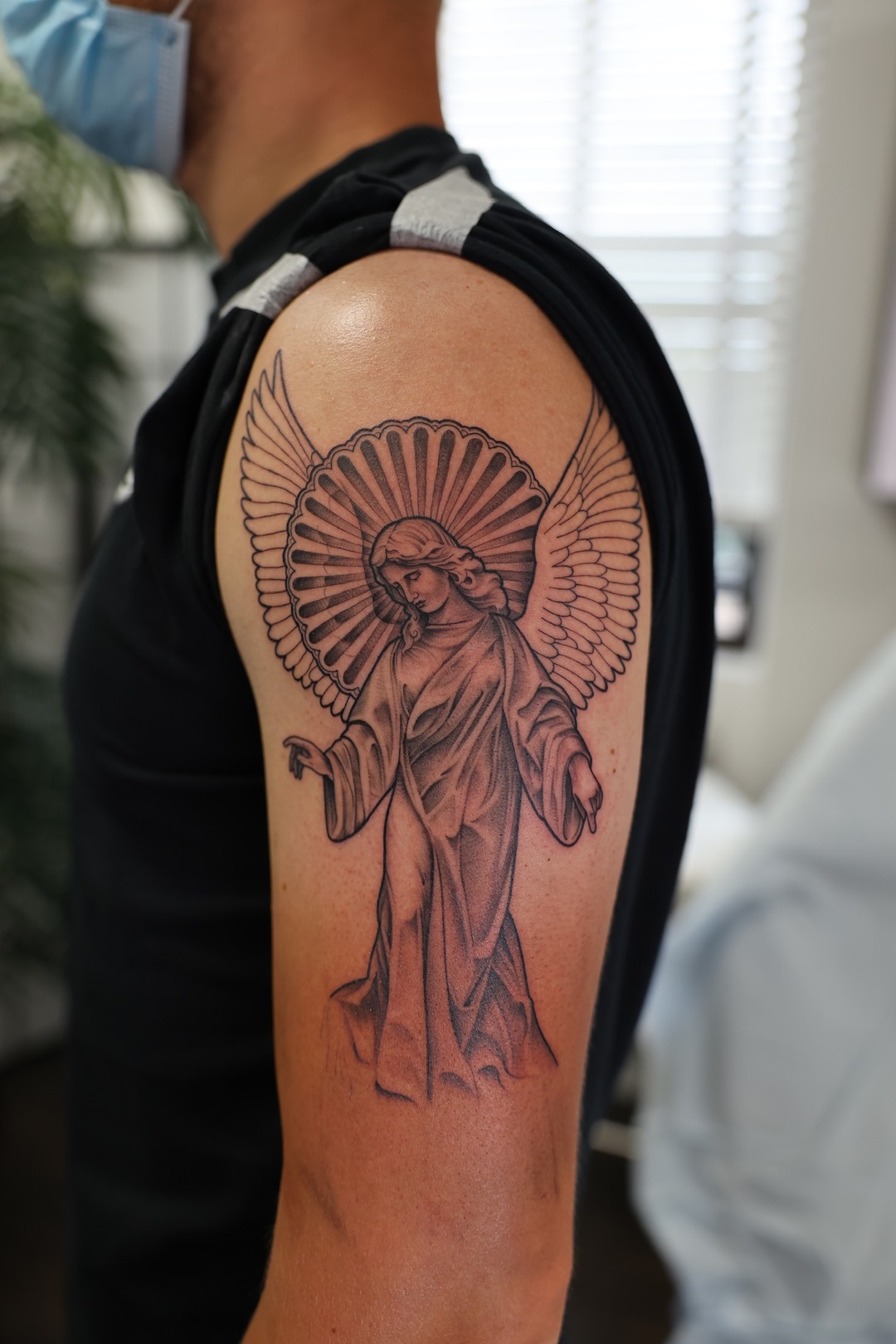 Guardian angel with radiant halo and spread wings, upper arm tattoo, black and grey by Matt Roe, Kensington London