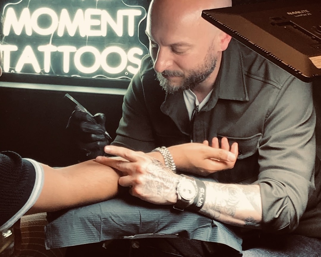 Matt Roe tattooing beside the In The Moment Tattoos neon