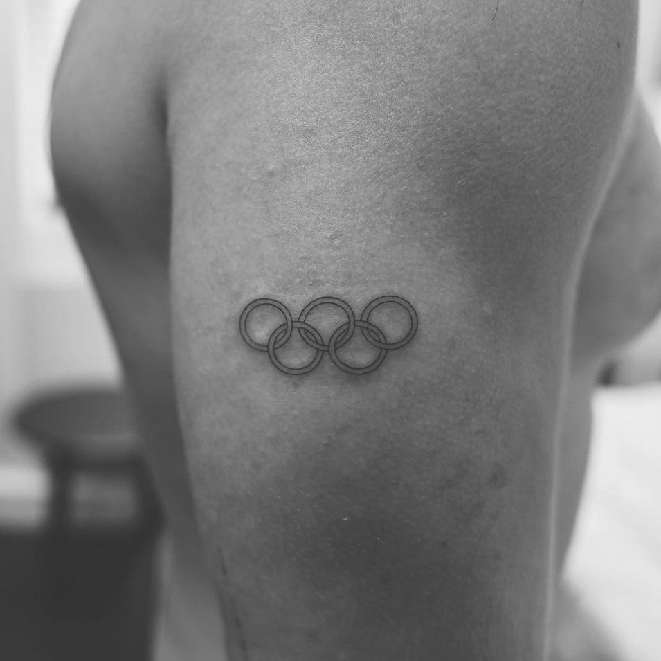Fine line Olympic rings tattoo on bicep by Matt Roe, London