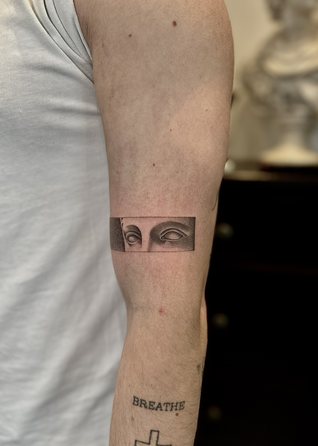 Sculpture eyes horizontal band upper arm tattoo, black and grey by Matt Roe, Kensington London