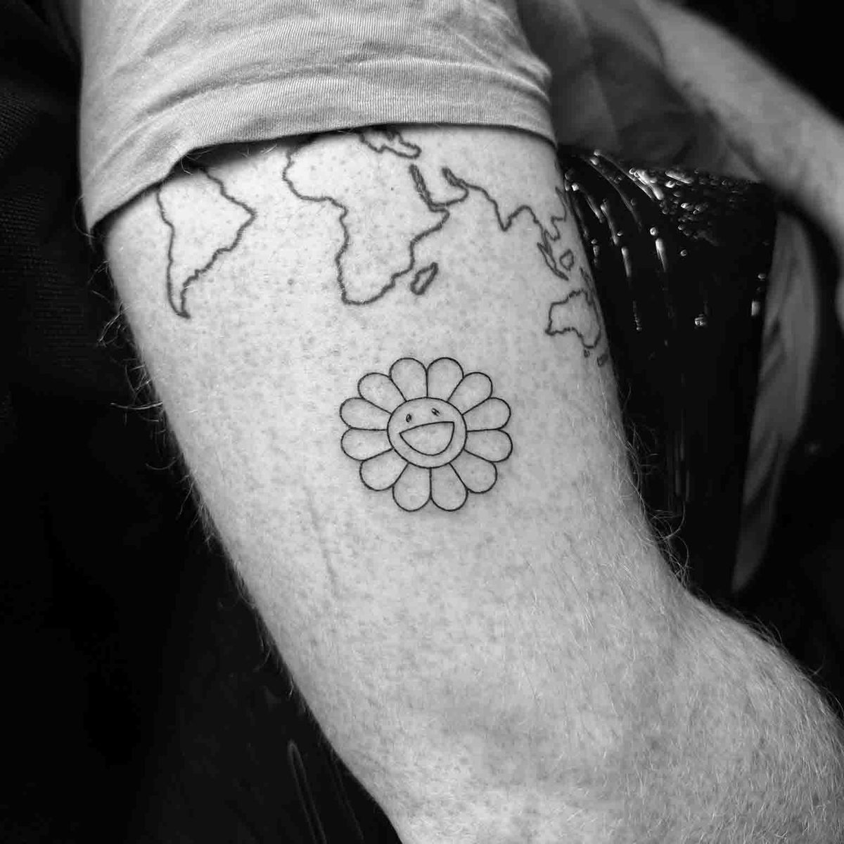 Fine line world map outline with smiley flower tattoo on forearm by Matt Roe, London